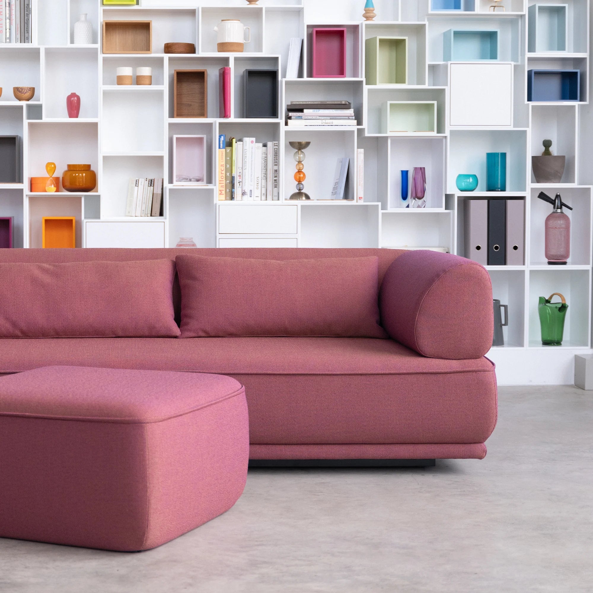 Dreisitzer Sofa Gordo in violett mit Kissen und Pouf vor weißem Regal